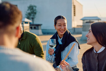 Obraz premium Diverse group of young adult friends enjoying a rooftop gathering, smiling and engaging in conversation while drinking wine