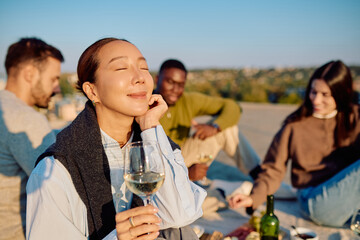 Diverse friends enjoying wine, snacks and sunset vibes at a rooftop picnic—golden-hour laughter, relaxation and urban togetherness