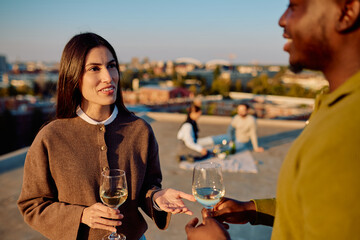 Diverse friends enjoying a urban sunset rooftop party, talking and drinking white wine, celebrating friendship and community