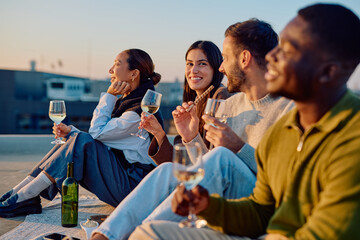 Diverse group of young adult friends relaxing on a city rooftop, drinking white wine and snacks at a sunset gathering
