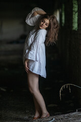 Naklejka premium Young woman in a flowing white dress stands confidently in an abandoned building, showcasing her stylish footwear and the contrast of light and shadow in the atmospheric setting