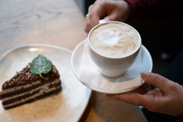Cup Of Fresh Cappuccino And Chocolate Layer Cake Served On Wooden Table In Cozy Cafe