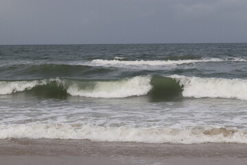 Ocean Waves Rolling toward Sandy Shore under Gray Sky with White Sea Foam