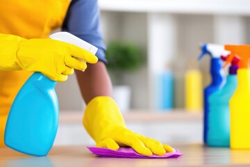 Person in yellow gloves cleaning a kitchen counter with a spray bottle and cloth, colorful cleaning supplies in background