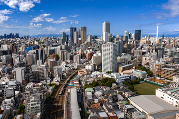 Fototapeta premium Daylight aerial view of Tokyo, Japan, shows a curving elevated railway in the foreground leading toward Shinjuku towers, with tightly packed buildings and clear visibility.