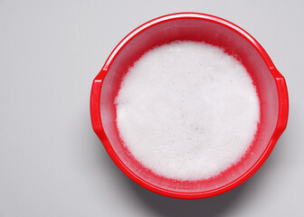 Red plastic basin with water and foam on grey background, top view