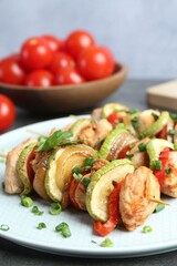 Tasty skewers with chicken, vegetables and green onion on grey table, closeup