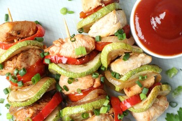 Tasty skewers with chicken, vegetables, sauce and green onion on plate, top view