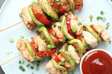 Tasty skewers with chicken, vegetables, sauce and green onion on plate, top view