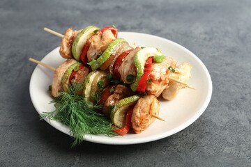 Tasty skewers with chicken, vegetables, dill and green onion on grey table, closeup