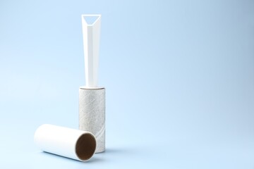 Lint roller with used sticky tape and new adhesive roll on light blue background, space for text