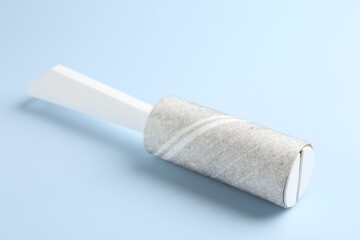 Lint roller with used sticky tape on light blue background, closeup