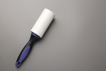 Lint roller with used sticky tape on grey background, top view. Space for text