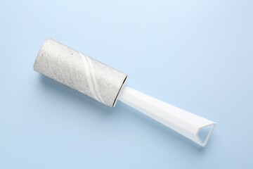 Lint roller with used sticky tape on light blue background, top view