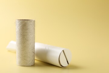 Lint roller and used adhesive roll on yellow background, closeup. Space for text