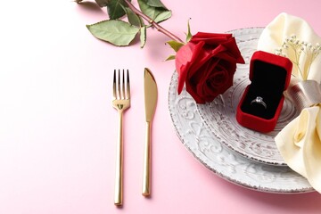 Beautiful table setting for romantic dinner, box with engagement ring and rose on pink background, closeup