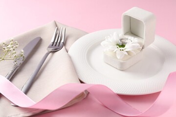 Beautiful table setting for romantic dinner and box with engagement ring on pink background, closeup
