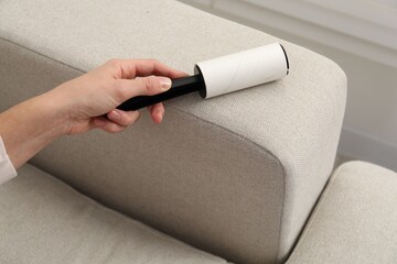 Woman cleaning sofa with lint roller at home, closeup