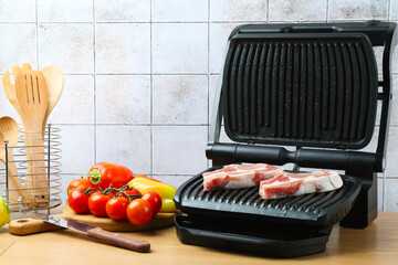 Electric grill with raw meat and vegetables on wooden table