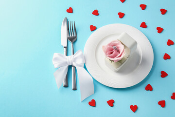 Beautiful table setting for romantic dinner, box with engagement ring and rose on light blue background, above view. Space for text