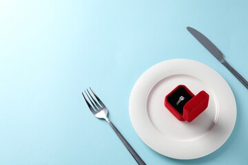 Beautiful table setting for romantic dinner and box with engagement ring on light blue background, above view. Space for text