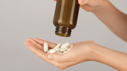 Close-up of a hand full of white tablets being poured from a brown glass bottle.