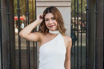 Stunning young woman in stylish white dress poses confidently against urban backdrop, radiating modern elegance and timeless beauty for fashion campaigns