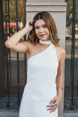 Stunning young woman in stylish white dress poses confidently against urban backdrop, radiating modern elegance and timeless beauty for fashion campaigns