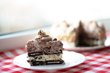Slice of chocolate cream cake on plate, blurred cake in background, natural light.