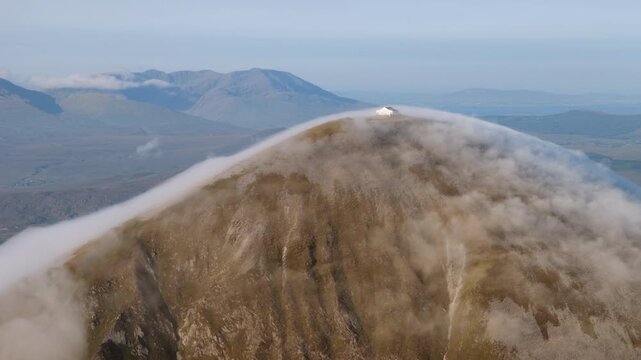 Amazing 4K aerial video of flying above and around Most Famous mountain in Ireland - Croagh Patrick in windy weather, with moving fog and clouds with breathtaking views around, Westport, Ireland
