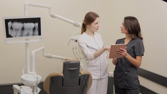 Two women dentist doctors are standing in a dental office and looking at a tablet