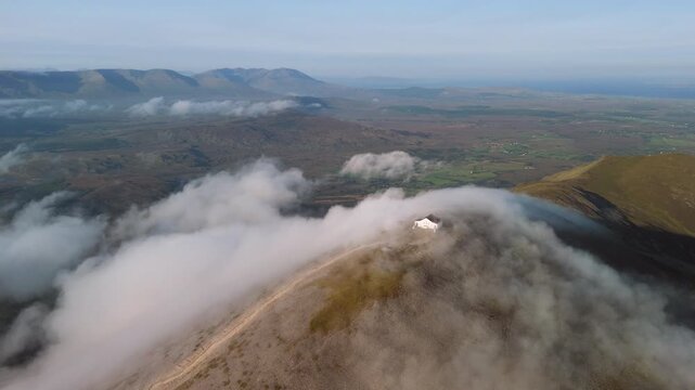 Amazing 4K aerial video of flying above and around Most Famous mountain in Ireland - Croagh Patrick in windy weather, with moving fog and clouds with breathtaking views around, Westport, Ireland