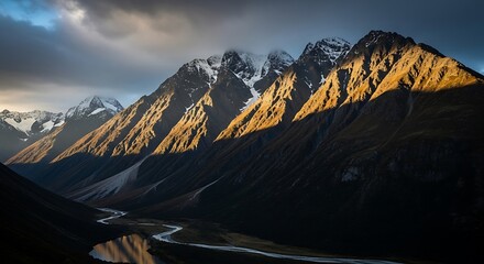Majestic mountain range bathed in golden sunlight, showcasing a winding river valley and snow-capped peaks.