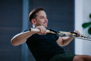 Man performs rowing exercise on reformer pilates machine in modern studio during morning workout session focused on strength and flexibility