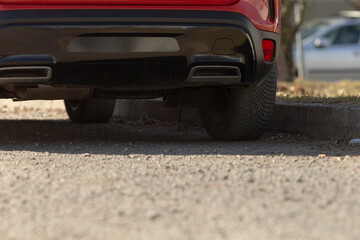 lowangle red bumper over gravel ground, rear undercarriage and tire edge framed against textured stones; earthy foreground contrasts glossy vehicle surface creating tactile, grounded automotive study