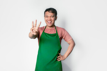 Asian young man wearing apron over white background showing and pointing up with fingers number three while smiling confident and happy.