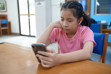 Teenage girl is sitting at a table , watching short videos or playing online game on her phone