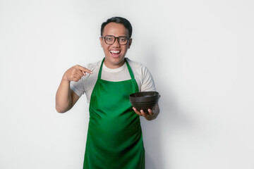 Smiling Asian man wearing green apron and glasses holding and pointing at black bowl