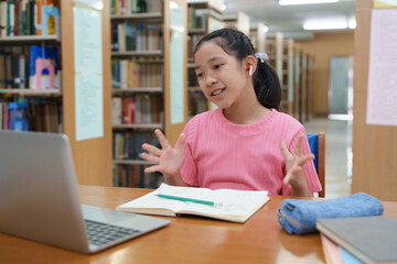 School student girl having video call on her computer in library at school.