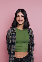 Smiling young woman poses confidently in front of a pink background wearing casual fashion during a...