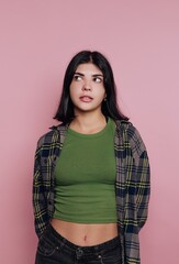 Young woman with dark hair poses in a green top and flannel shirt against a pink background