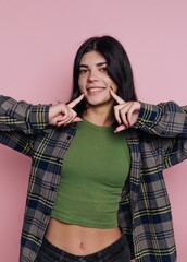 Young woman smiles playfully while posing in casual outfit against a pink background