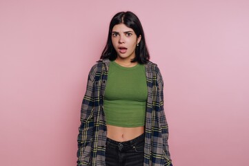 Young woman with dark hair expressing surprise against a pink background in casual clothing
