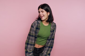 Young woman poses playfully in a casual outfit against a pink background during a personal photo...