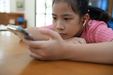 Teenage girl is sitting at a table , watching short videos or playing online game on her phone