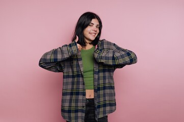 Smiling young woman giving thumbs up in cozy plaid shirt against soft pink background