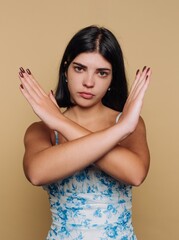 Fototapeta premium Young woman in floral dress expresses strong emotions with crossed arms against a neutral backdrop