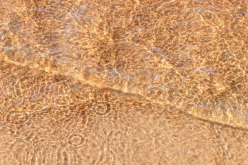 A close view of shallow, sunlit water over wet sand creating intricate ripple patterns