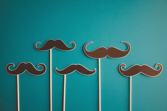 Variety of black mustache photo booth props on sticks against a vibrant teal background for Movember and men's health events