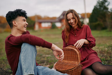 Genuine young couple enjoying a relaxed outdoor picnic, sharing laughter and candid interaction beside a woven basket; natural poses, warm tones and truthful emotion convey a sense of real connection.